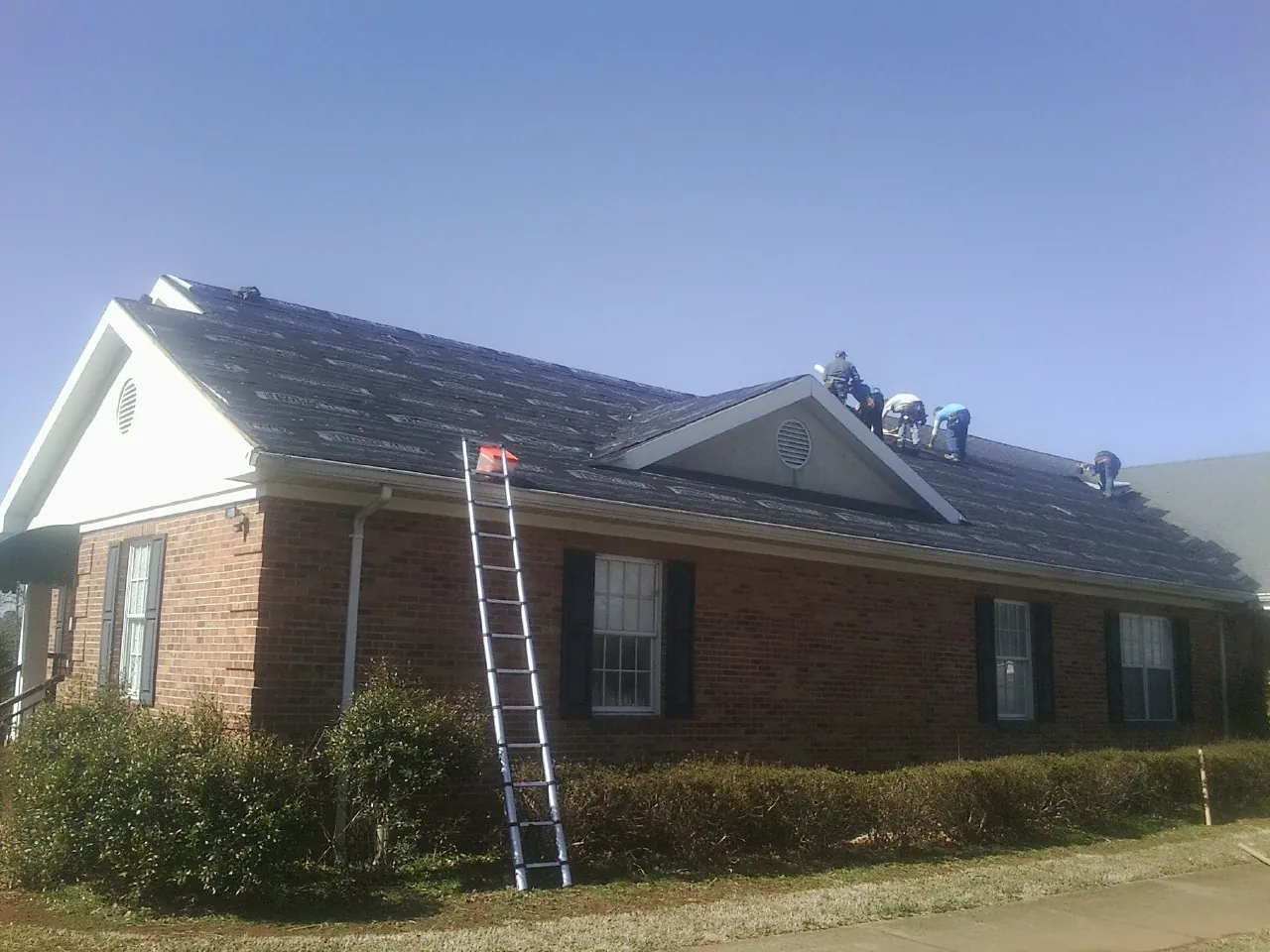 Crew tearing shingles off a brick ranch roof with a ladder set — Metal Roof Repair work by our crew in Columbiana