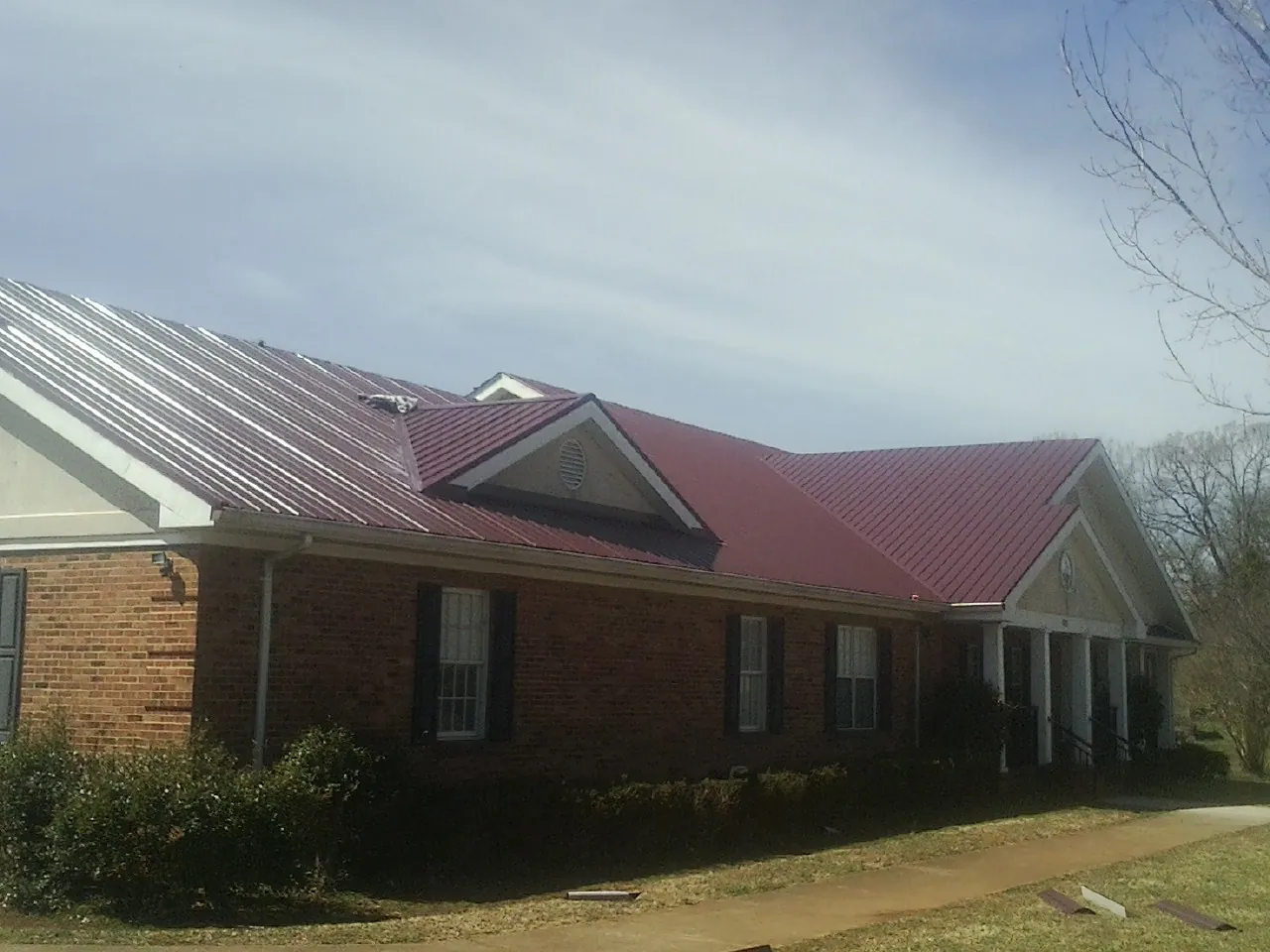 Red metal roof with gabled entries on a long brick building, from a Hail Damage Roof Repair job in Columbiana