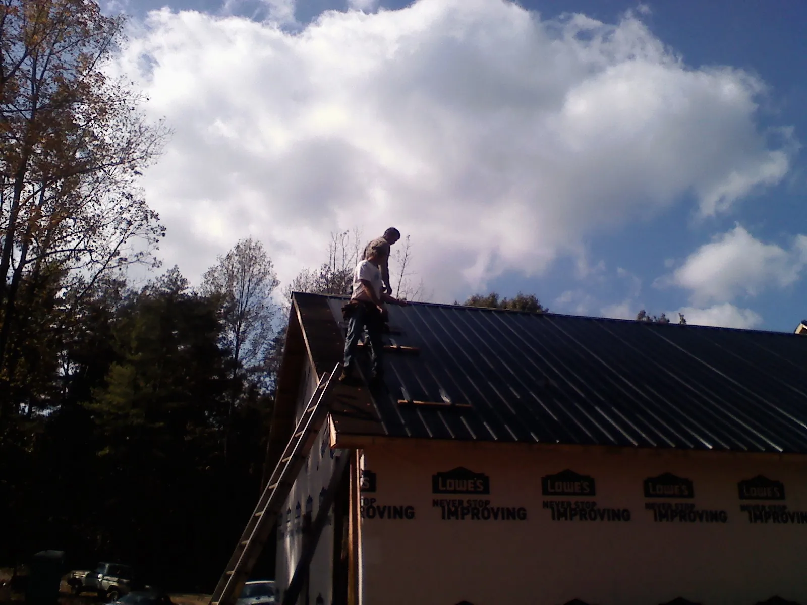 Roofer fastening dark metal panels high against a cloudy sky, from a Roof Inspection job in Columbiana